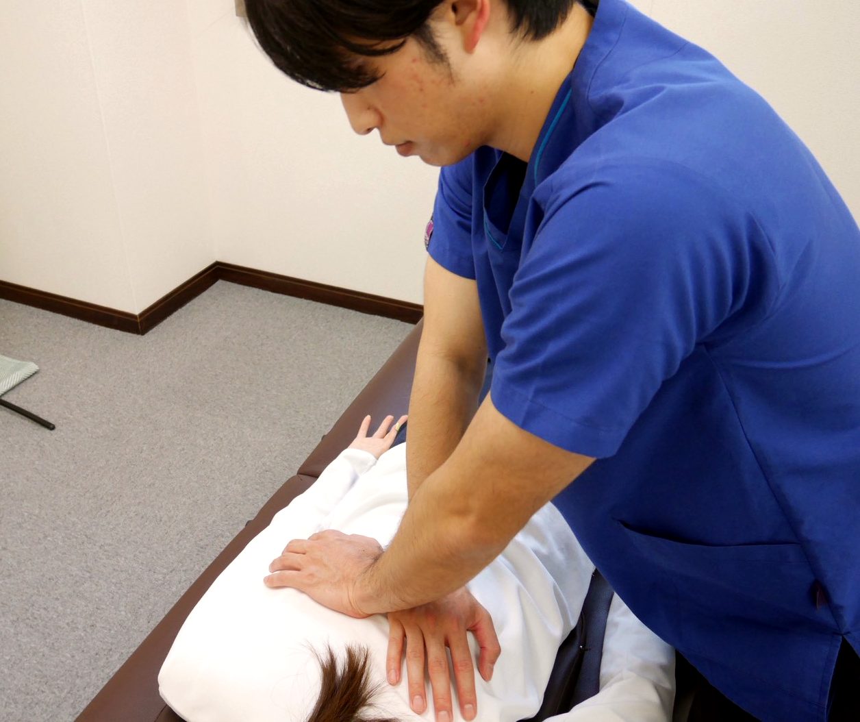 産後の腰・骨盤まわりの施術：うつ伏せの患者さんの背中と腰に両手をあて、やさしい刺激で施術する様子