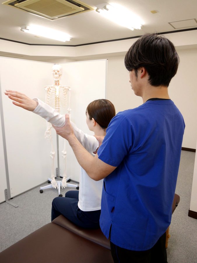 骨格模型を使いながら肩の動きを検査する小林院長